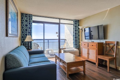 Living area with a textured wall, a textured ceiling, a wall of windows, and wood finished floors