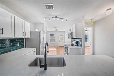 Kitchen with tasteful backsplash, white cabinets, appliances with stainless steel finishes, a textured ceiling, and light wood finished floors