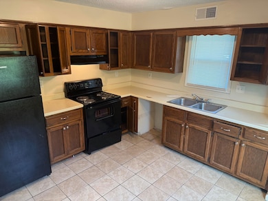 Kitchen with black appliances, under cabinet range hood, open shelves, light countertops, and a textured ceiling