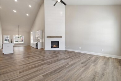 Unfurnished living room featuring ceiling fan, a chandelier, a fireplace, high vaulted ceiling, and wood finished floors