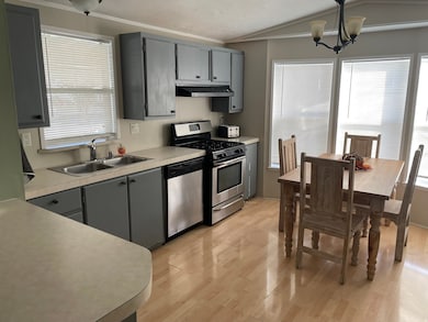 Kitchen with gray cabinetry, stainless steel appliances, a chandelier, light wood-type flooring, and light countertops