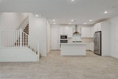 Kitchen featuring white cabinetry, an island with sink, stainless steel fridge, recessed lighting, and wall chimney exhaust hood