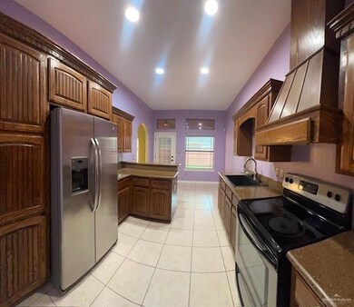 Kitchen with kitchen peninsula, electric range, light tile patterned floors, stainless steel fridge with ice dispenser, and sink