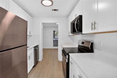 Kitchen featuring stainless steel appliances, light wood-style floors, white cabinets, and light stone countertops