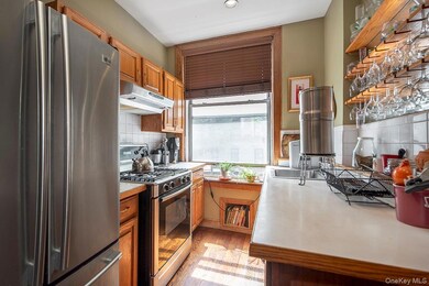 Kitchen with appliances with stainless steel finishes, light countertops, under cabinet range hood, light wood-style flooring, and brown cabinetry