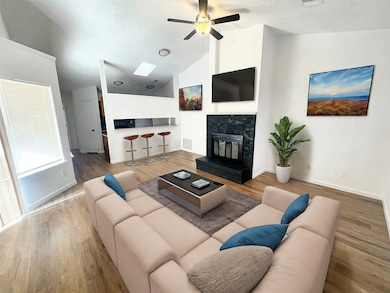 Living room with light wood-style floors, a glass covered fireplace, ceiling fan, a textured ceiling, and high vaulted ceiling