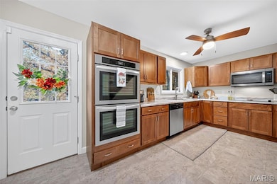 Kitchen with stainless steel appliances, light countertops, brown cabinetry, and a ceiling fan
