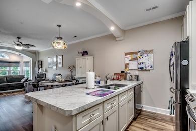 Kitchen with ornamental molding, light countertops, open floor plan, white cabinetry, and appliances with stainless steel finishes