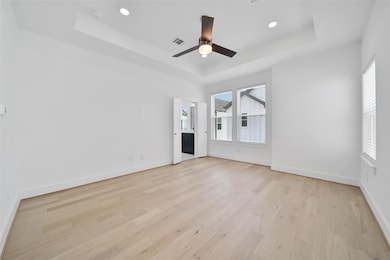 Bright, spacious room with light wood flooring and large windows. Features a recessed ceiling with a modern fan and ample natural light.