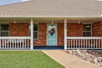 View of exterior entry featuring covered porch, brick siding, and a shingled roof