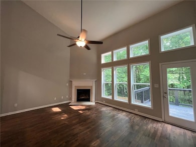 Unfurnished living room with a towering ceiling, dark wood finished floors, baseboards, a fireplace, and a ceiling fan