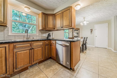Kitchen with brown cabinetry, tasteful backsplash, a textured ceiling, stainless steel dishwasher, and light tile patterned floors