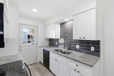 Kitchen with black appliances, light stone countertops, white cabinets, light wood finished floors, and recessed lighting