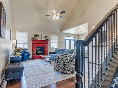 Living room with stairway, wood finished floors, high vaulted ceiling, a ceiling fan, and a brick fireplace