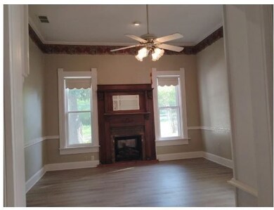Unfurnished living room featuring crown molding, wood finished floors, a glass covered fireplace, and ceiling fan