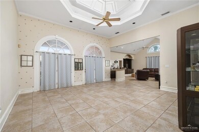 Tiled entryway with crown molding, ceiling fan, a high ceiling, and a raised ceiling