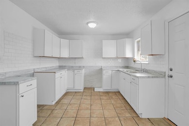 Kitchen with a textured ceiling, tasteful backsplash, light tile patterned floors, and white cabinetry