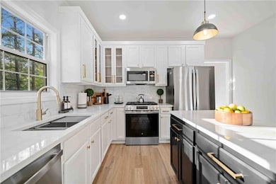 Kitchen with stainless steel appliances, a sink, white cabinetry, light countertops, and light wood-type flooring