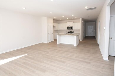 Kitchen featuring appliances with stainless steel finishes, a sink, light countertops, light wood-type flooring, and an island with sink