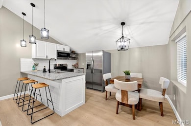 Kitchen with appliances with stainless steel finishes, vaulted ceiling, decorative backsplash, hanging light fixtures, and a peninsula