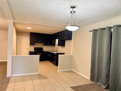 Kitchen with black appliances, dark cabinets, a textured ceiling, a sink, and light countertops