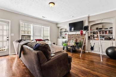 Living room featuring a textured ceiling, ornamental molding, wood finished floors, and built in features