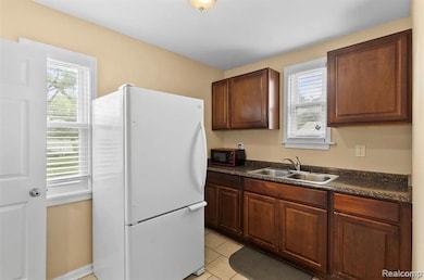 Kitchen with dark countertops, freestanding refrigerator, light tile patterned flooring, and black microwave
