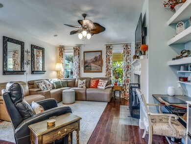 Living room featuring dark wood-style flooring, healthy amount of natural light, a fireplace with flush hearth, and ceiling fan