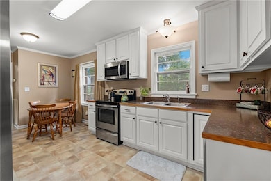 Kitchen featuring stainless steel appliances, white cabinetry, crown molding, and lots of natural light