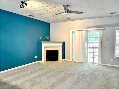 Living room with carpet floors, a textured ceiling, a fireplace with flush hearth, and a ceiling fan