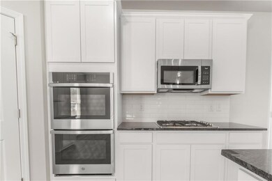Kitchen featuring appliances with stainless steel finishes, backsplash, dark stone countertops, and white cabinetry