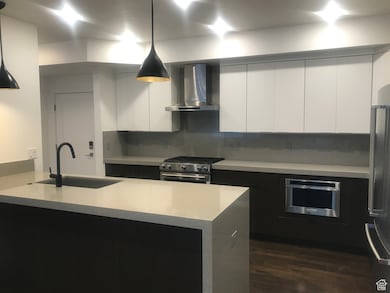 Kitchen with modern cabinets, wall chimney exhaust hood, appliances with stainless steel finishes, pendant lighting, and light countertops