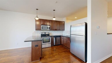 Kitchen featuring appliances with stainless steel finishes, hanging light fixtures, decorative backsplash, dark wood-type flooring, and a breakfast bar