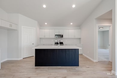 Kitchen featuring an island with sink, white cabinetry, stainless steel appliances, light wood-style floors, and recessed lighting