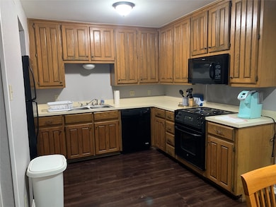 Kitchen with black appliances, light countertops, brown cabinetry, and dark wood-style floors