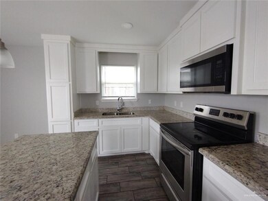 Kitchen with stainless steel appliances, a sink, white cabinets, and light stone countertops