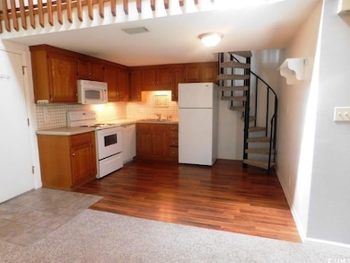 Kitchen with white appliances, tasteful backsplash, brown cabinets, and light countertops
