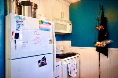 Kitchen featuring white appliances, wainscoting, and white cabinets