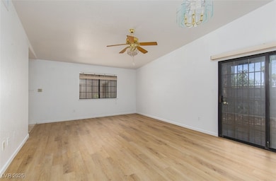 Empty room featuring light wood-type flooring, a ceiling fan, lofted ceiling, and a chandelier
