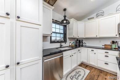 Kitchen with dishwasher, dark wood-type flooring, lofted ceiling, hanging light fixtures, and white cabinetry