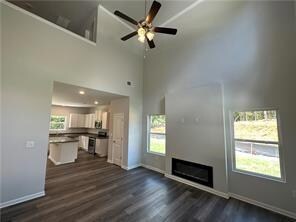 Unfurnished living room with dark wood finished floors, ceiling fan, a high ceiling, and a fireplace