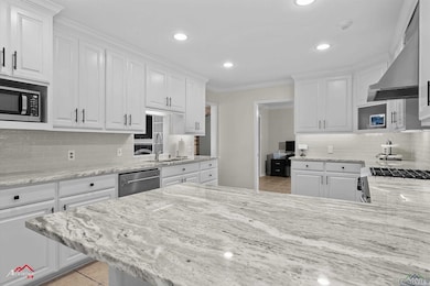 Kitchen with light tile patterned flooring, white cabinets, tasteful backsplash, light stone counters, and crown molding