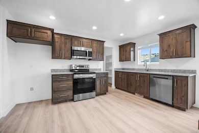 Kitchen featuring stainless steel appliances, dark brown cabinetry, recessed lighting, light wood-style flooring, and light stone countertops