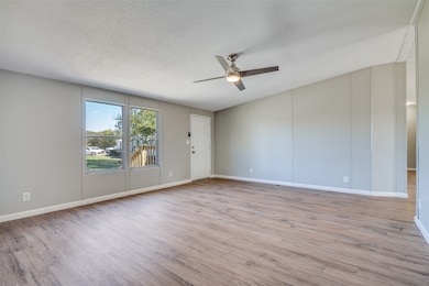 Empty room with light wood-style floors, a textured ceiling, and a ceiling fan