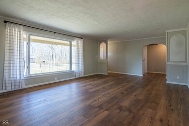 empty room featuring baseboards, arched walkways, dark wood finished floors, and crown molding