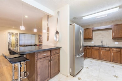 Kitchen featuring freestanding refrigerator, brown cabinets, dark countertops, a breakfast bar, and a textured ceiling