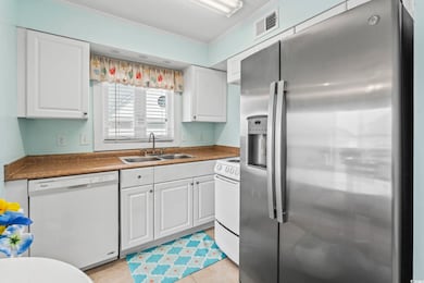 Kitchen featuring white appliances, crown molding, white cabinetry, dark countertops, and light tile patterned floors