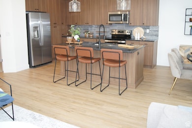Kitchen featuring stainless steel appliances, decorative backsplash, brown cabinetry, and a kitchen bar