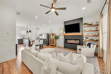 Living area featuring ceiling fan, a large fireplace, light wood finished floors, and recessed lighting
