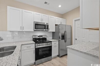 Kitchen featuring appliances with stainless steel finishes, a sink, white cabinetry, light stone counters, and recessed lighting